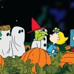 Peanuts characters in Halloween costumes standing in a pumpkin patch at night.