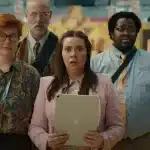Four coworkers from Apple’s “Underdogs” ad look shocked while holding an iPad at a tech convention.