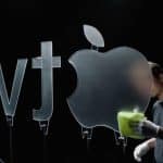 Person cleaning a large glass Apple TV logo under studio lighting.