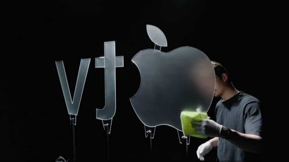 Person cleaning a large glass Apple TV logo under studio lighting.