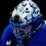 Hockey goalie wearing a blue jersey and a detailed wolf-themed goalie mask.