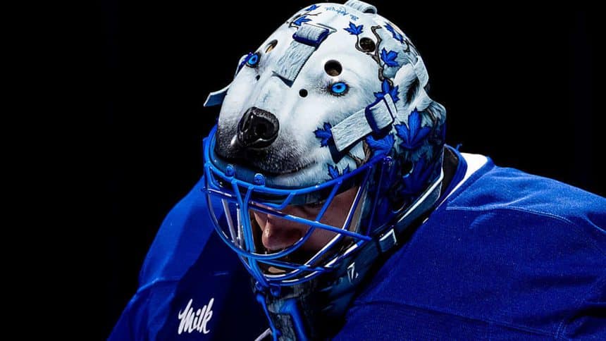 Hockey goalie wearing a blue jersey and a detailed wolf-themed goalie mask.
