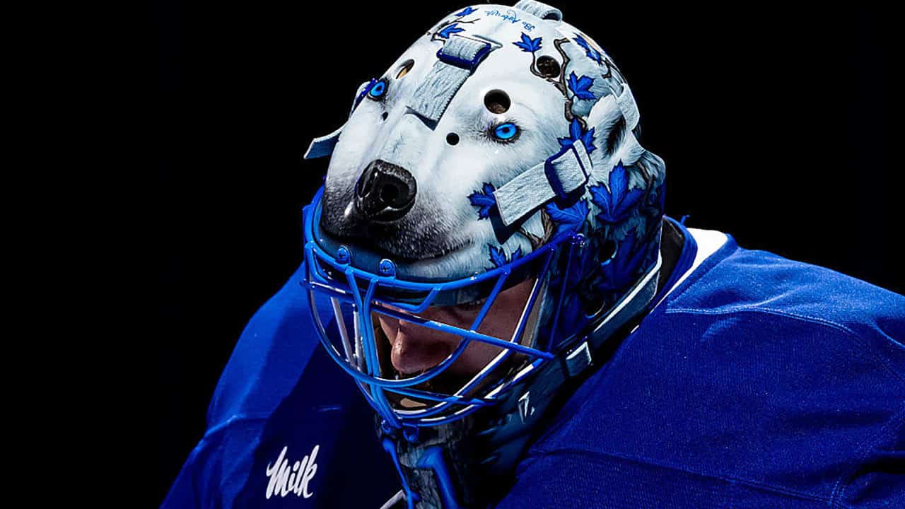 Hockey goalie wearing a blue jersey and a detailed wolf-themed goalie mask.