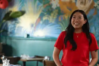 Awkwafina smiling while standing in a colourful restaurant setting.
