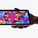 A hand holding an iPad mini displaying vibrant digital artwork.