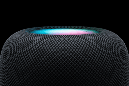 Close-up of Apple’s HomePod mini speaker glowing with colourful light on top.