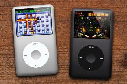Two classic iPods, one silver and one black, displaying games on their screens on a wooden surface.