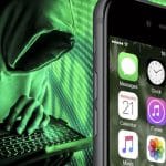 A hacker in a hoodie typing on a laptop next to an iPhone screen.