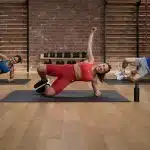 Three Apple Fitness+ trainers doing a side plank exercise in a studio.