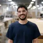 Man wearing safety glasses smiling in a manufacturing workshop.