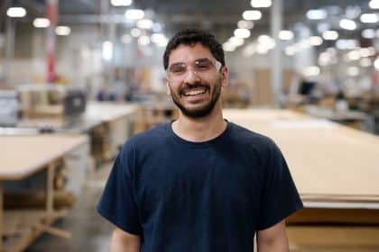 Man wearing safety glasses smiling in a manufacturing workshop.