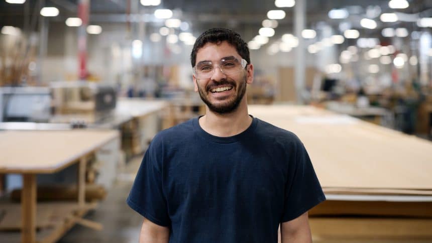 Man wearing safety glasses smiling in a manufacturing workshop.