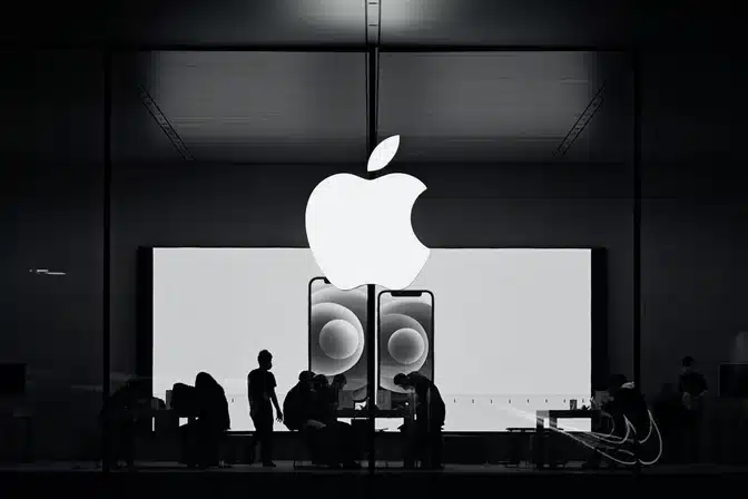 Silhouettes of people inside an Apple Store beneath a large Apple logo.