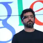 Sergey Brin wearing Google Glass in front of a Google logo.