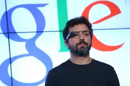 Sergey Brin wearing Google Glass in front of a Google logo.