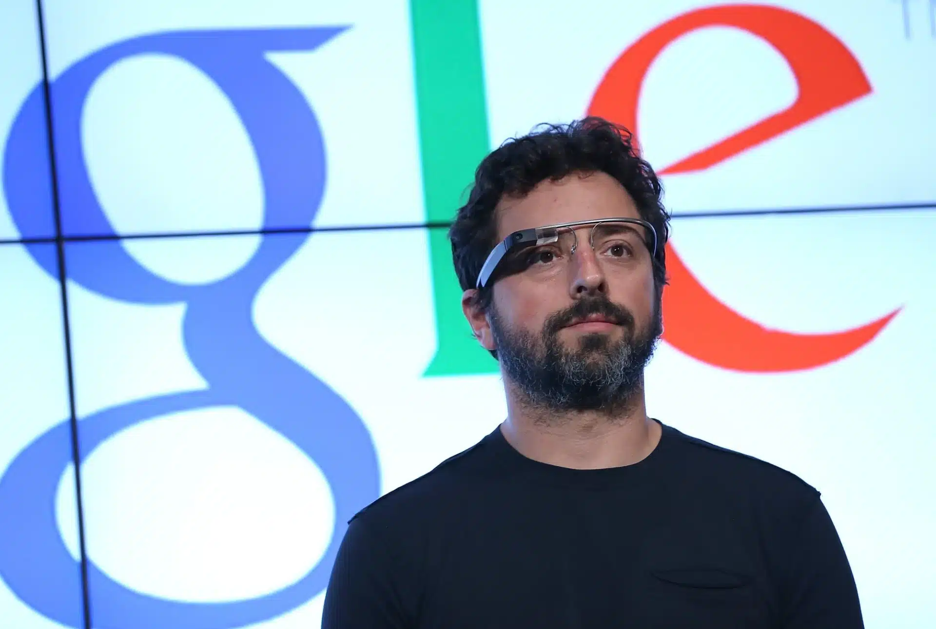 Sergey Brin wearing Google Glass in front of a Google logo.