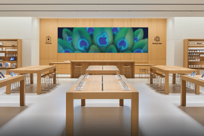 Apple Noida store interior with wooden tables, product displays, and a central video wall.