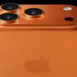 Close-up of an orange iPhone with triple rear cameras.