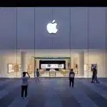 Apple Store exterior with illuminated logo and people outside at night.