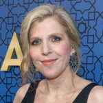 Woman smiling at an event with a blue patterned backdrop.