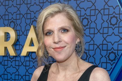 Woman smiling at an event with a blue patterned backdrop.