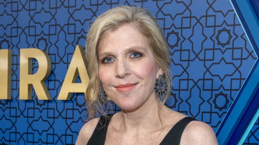 Woman smiling at an event with a blue patterned backdrop.