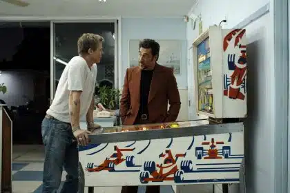 Two men talking while playing a racing-themed pinball machine.