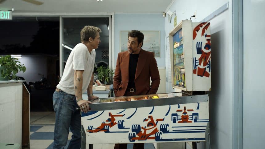 Two men talking while playing a racing-themed pinball machine.