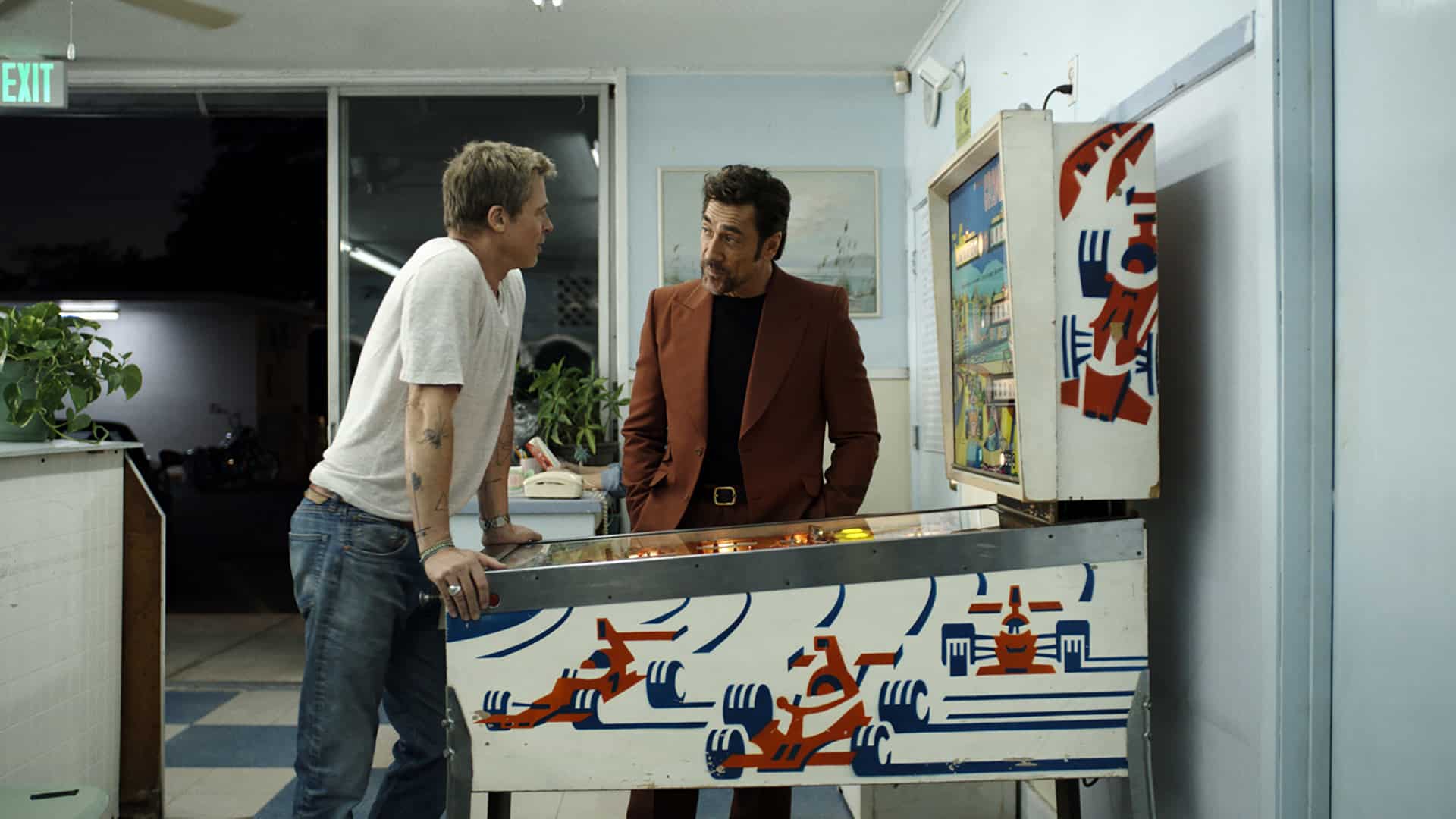Two men talking while playing a racing-themed pinball machine.