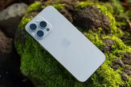 Silver iPhone with triple camera resting on moss-covered rocks outdoors.