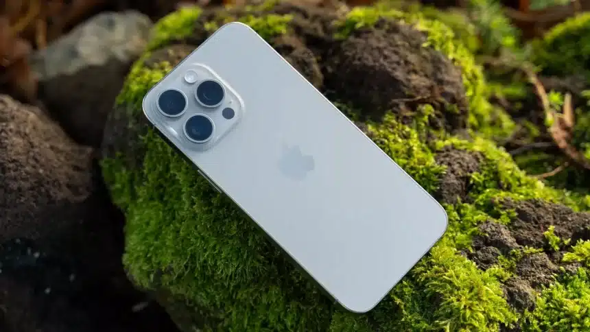 Silver iPhone with triple camera resting on moss-covered rocks outdoors.