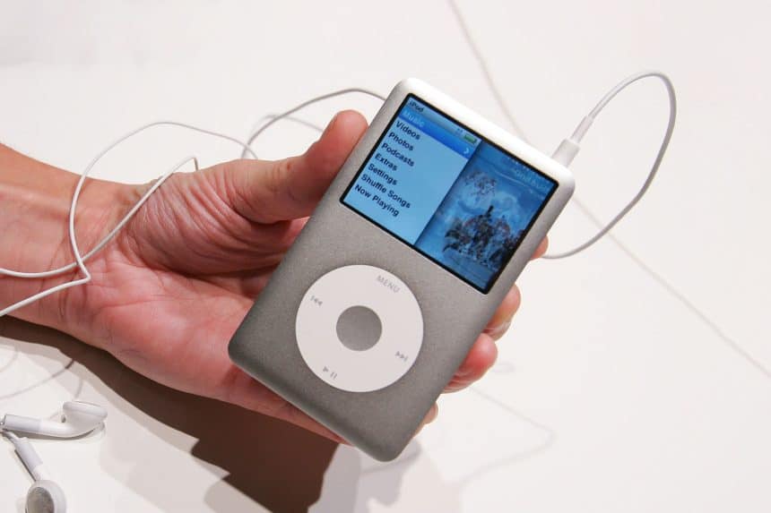 Hand holding a classic iPod with earphones attached.