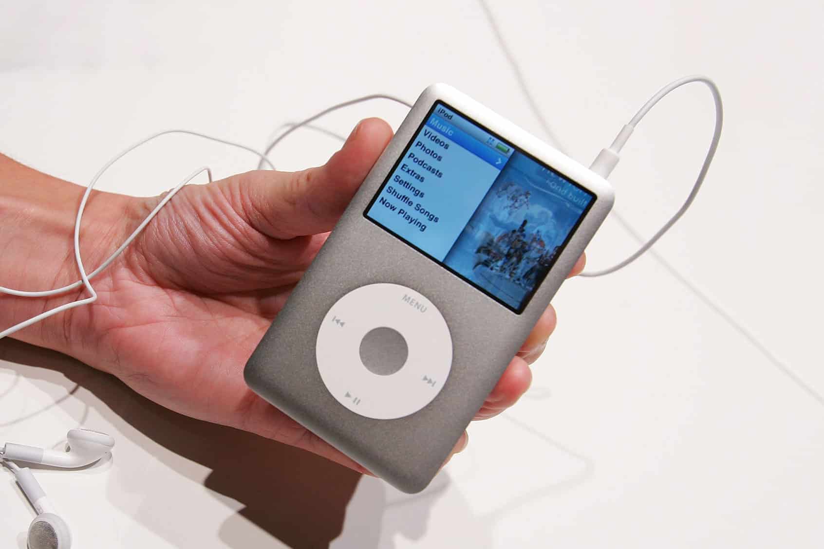 Hand holding a classic iPod with earphones attached.