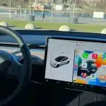 Tesla dashboard with steering wheel and center screen showing Apple CarPlay interface