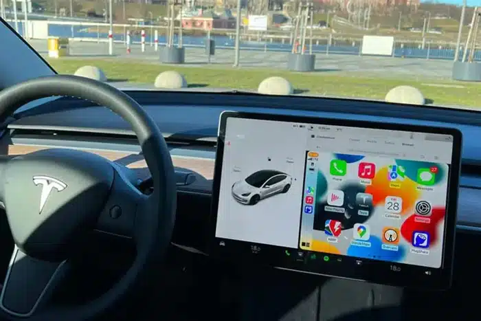 Tesla dashboard with steering wheel and center screen showing Apple CarPlay interface
