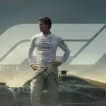 Formula 1 driver standing beside a race car in movie poster.
