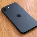 Black iPhone lying face down on a wooden table.