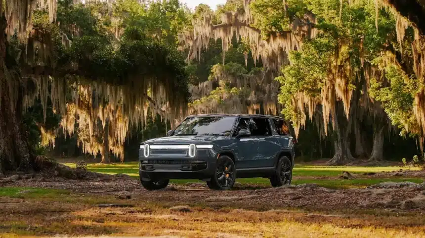 Rivian electric SUV parked in a forest clearing surrounded by trees.