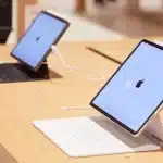 Two iPads on display stands connected to keyboards on a wooden table.