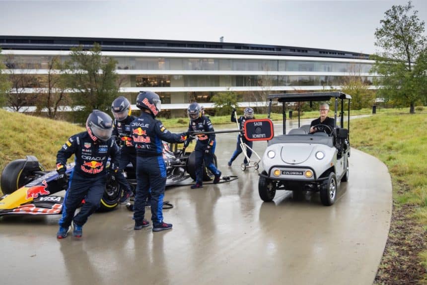 Red Bull F1 pit crew beside a race car as Tim Cook drives a golf cart at Apple Park.