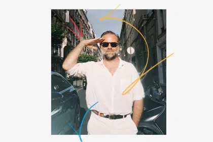 Man wearing sunglasses saluting on a city street with colourful graphic lines.