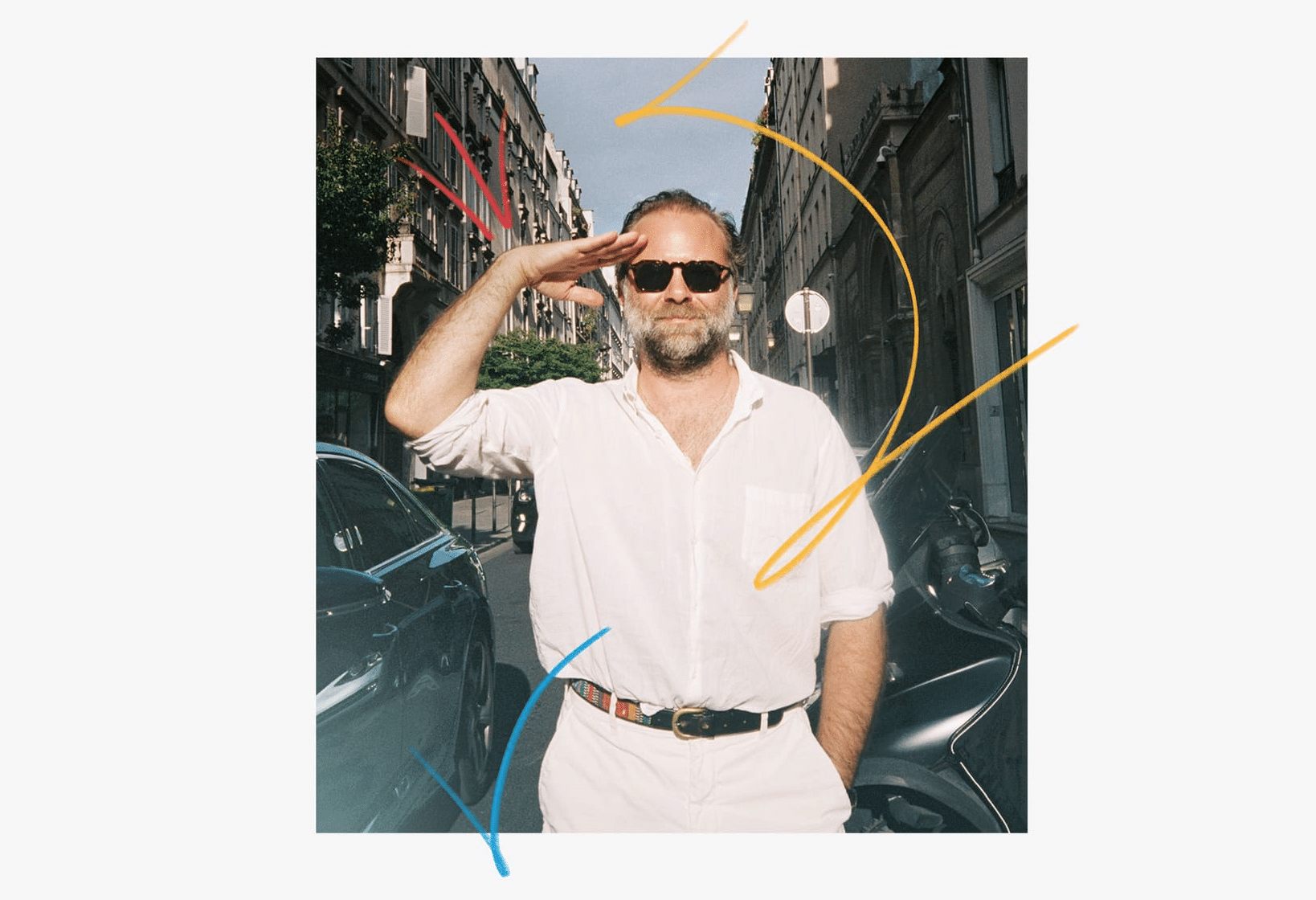 Man wearing sunglasses saluting on a city street with colourful graphic lines.