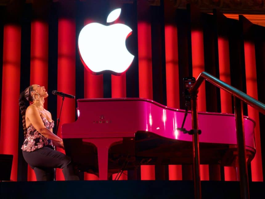 Alicia Keys performing at a pink piano under a glowing Apple logo.