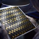 Person holding a circuit board with gold components under a light.