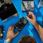 Person repairing a smartphone with tools on a workbench.