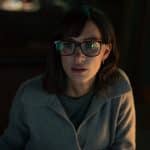 Woman with glasses focused on a computer screen in dim light.