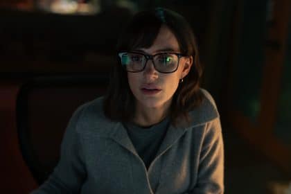 Woman with glasses focused on a computer screen in dim light.