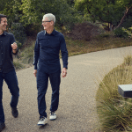 Two men walking and talking on a garden path outdoors.