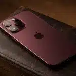 Red iPhone with triple cameras on a leather surface.