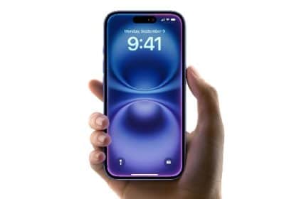 Hand holding an iPhone displaying the home screen.